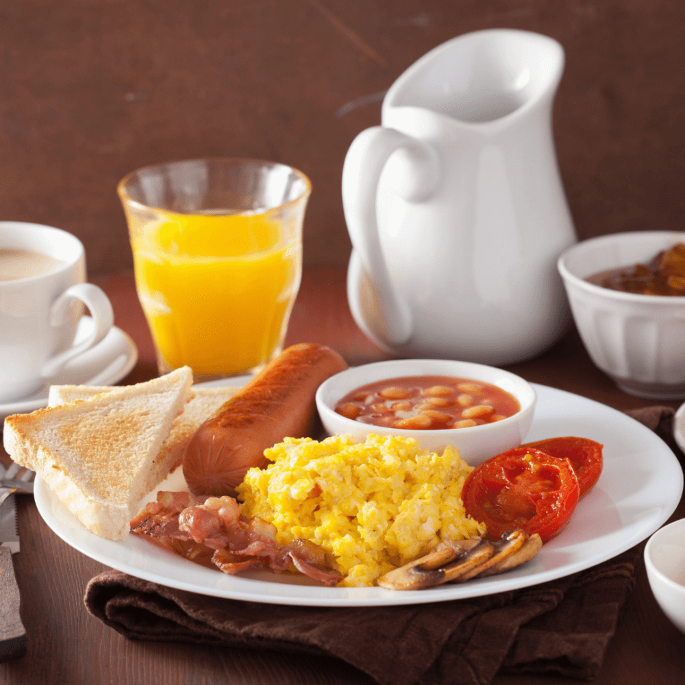 A breakfast plate with scrambled eggs, sausage, toast, beans, tomato, mushrooms, a glass of orange juice, and a cup of coffee. - Home Instead