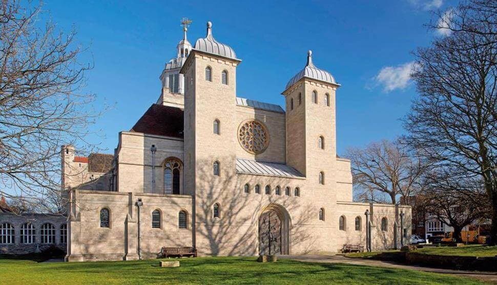 A large stone church with towers and a rose window, surrounded by trees and a grassy lawn under a clear blue sky. - Home Instead