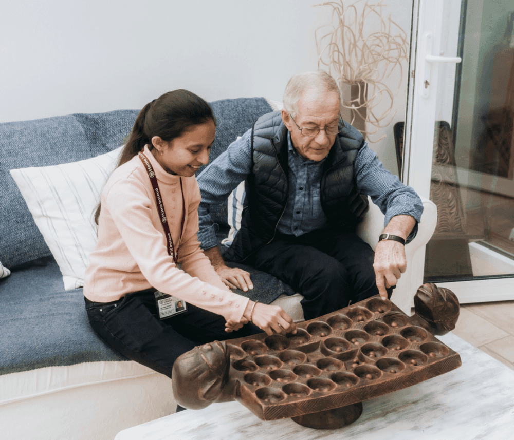 Elderly man and young girl playing a board game together on a coffee table in a cozy living room. - Home Instead