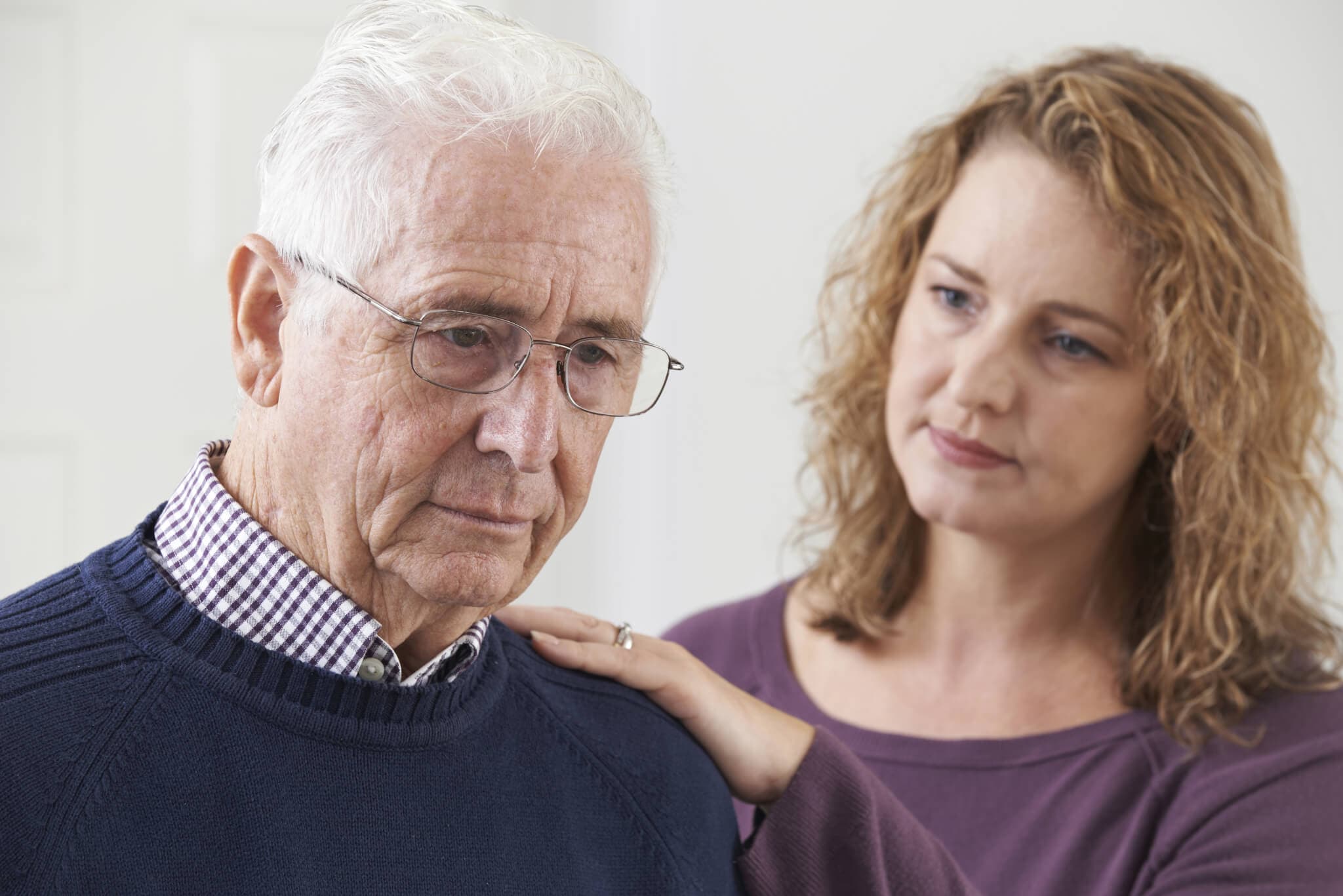 A concerned woman gently touches the shoulder of an elderly man who appears pensive. - Home Instead