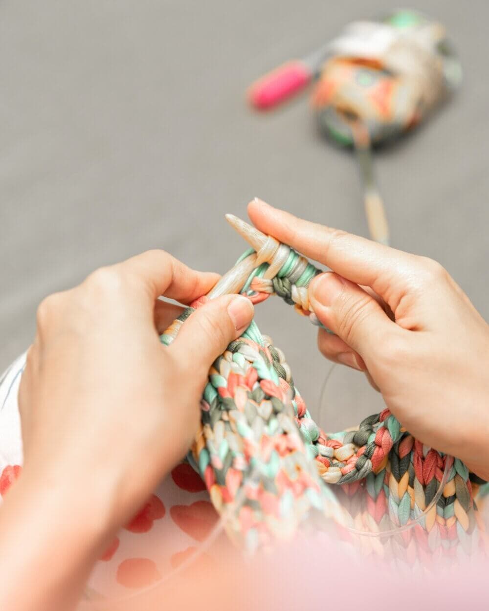 Close-up of hands knitting multicolored yarn with needles, with a ball of yarn in the background. - Home Instead