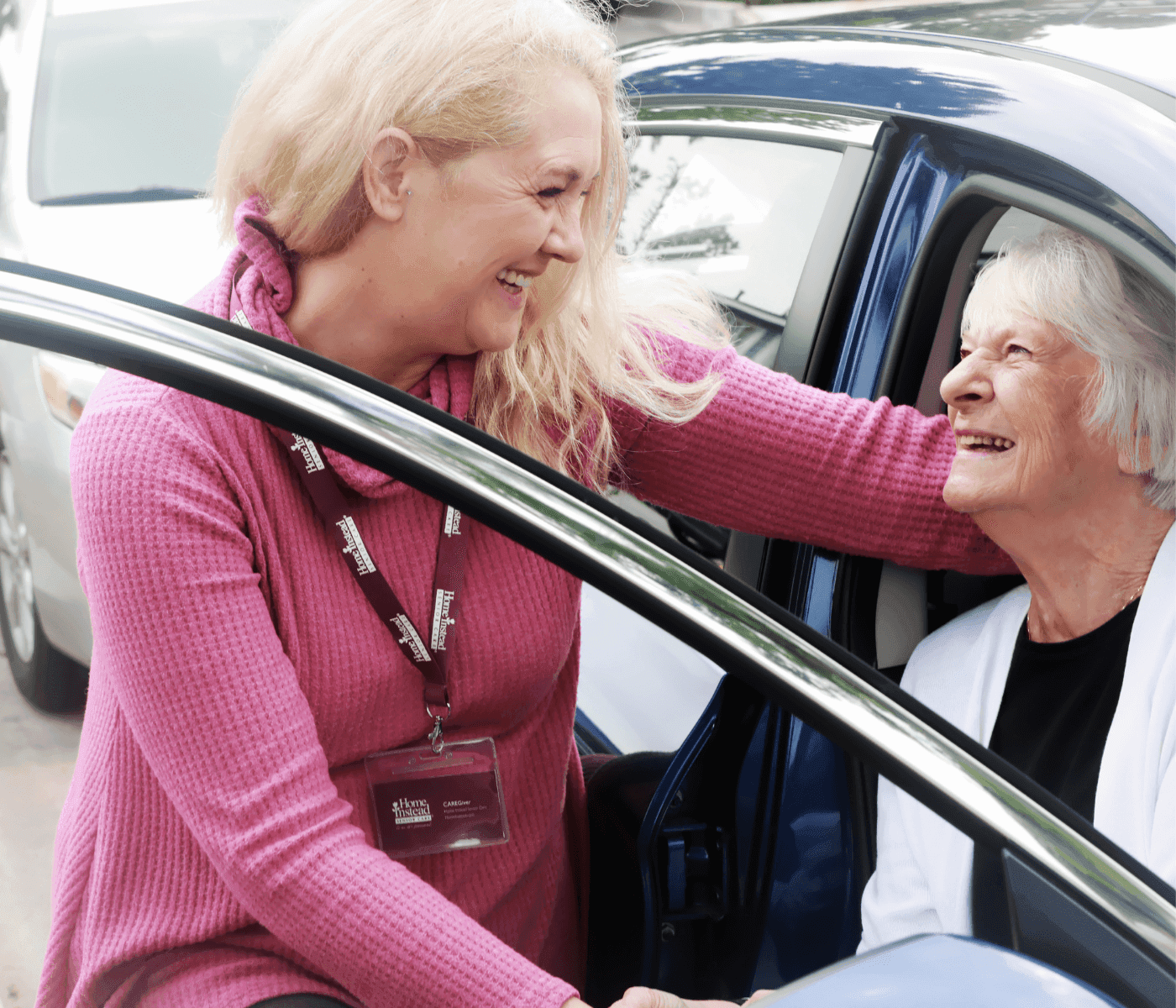A caregiver helps an elderly woman out of a car while they both smile warmly at each other. - Home Instead