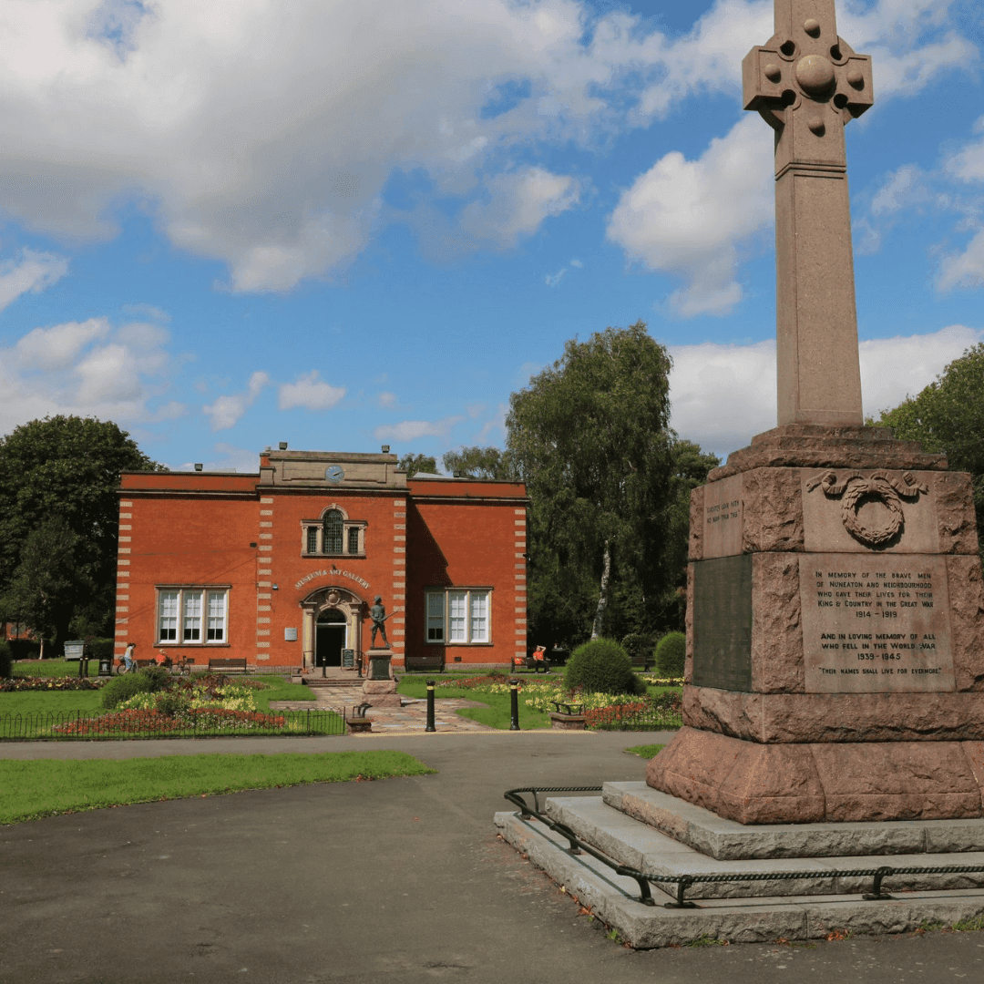 A brick building and a tall monument with inscriptions surrounded by greenery under a blue sky with clouds. - Home Instead