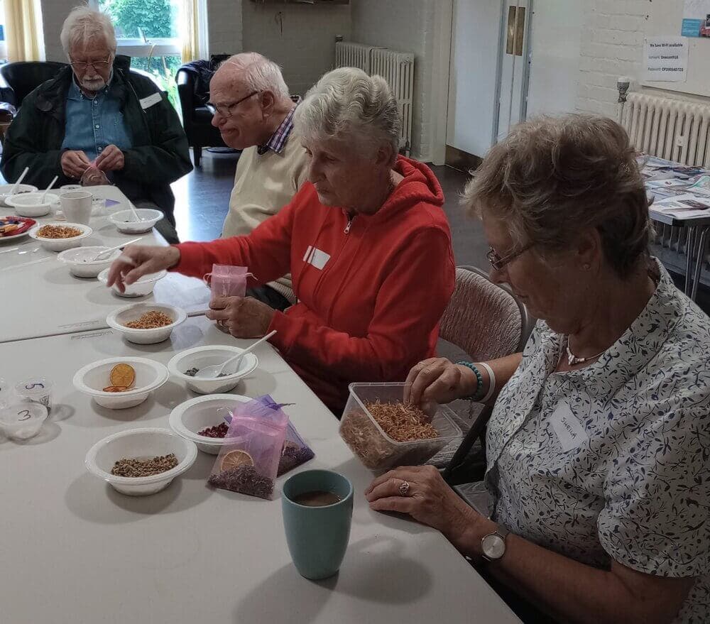 Four elderly individuals are seated at a table, sorting various seeds and grains into bowls. - Home Instead