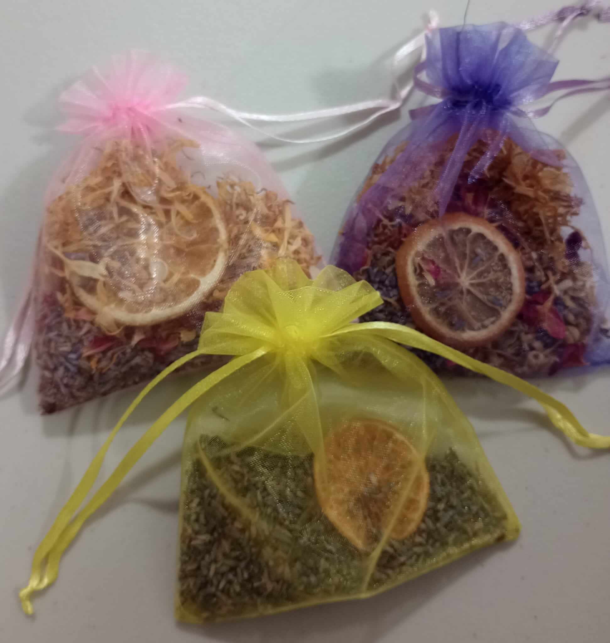 Three small organza bags in pink, purple, and yellow, filled with dried herbs and slices of dried citrus. - Home Instead