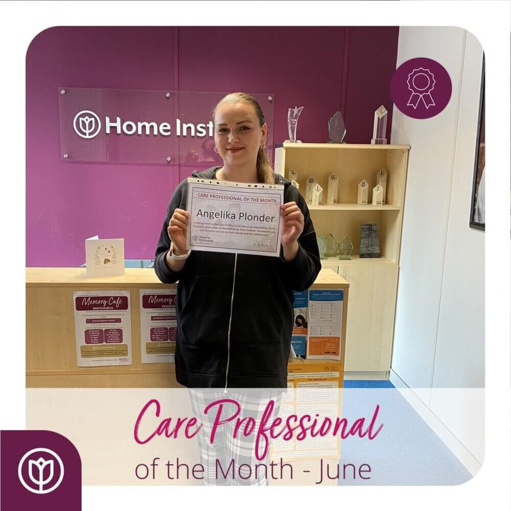 A person holding a "Care Professional of the Month - June" certificate stands in a room with a purple background. - Home Instead