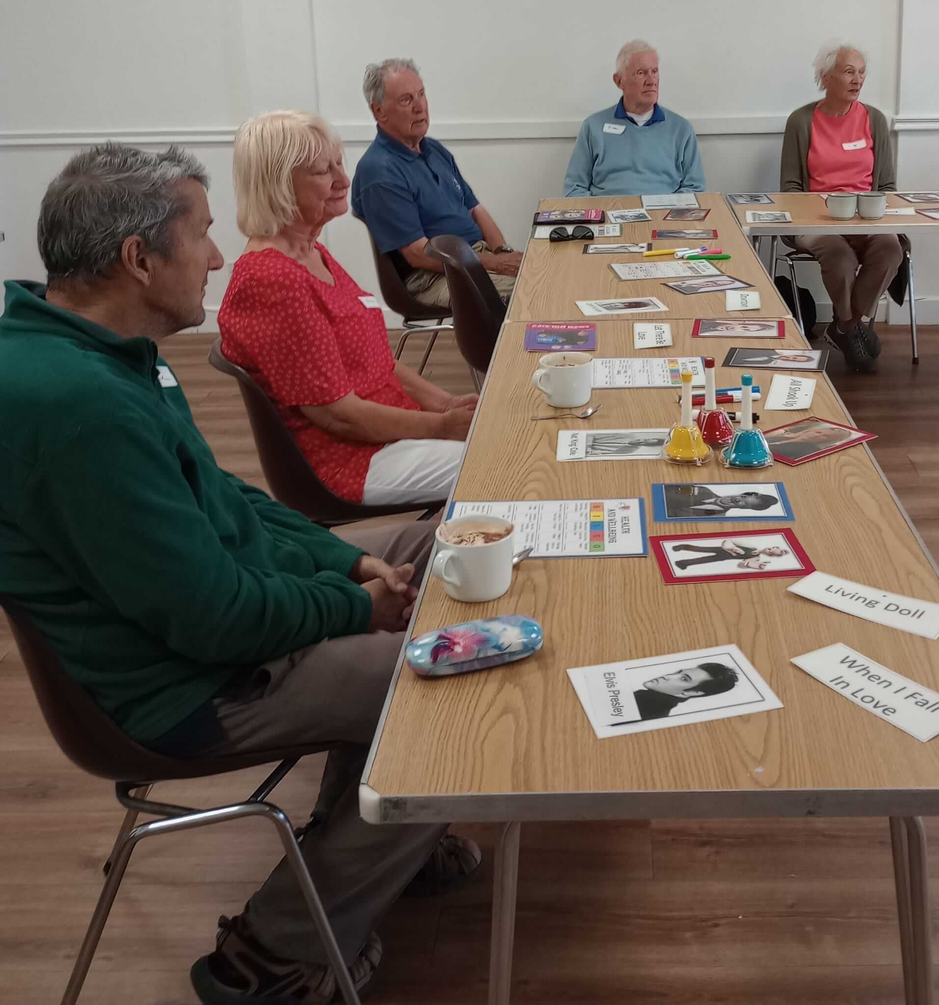 A group of elderly people sit around a table with photos, notes, and small lab equipment laid out. - Home Instead
