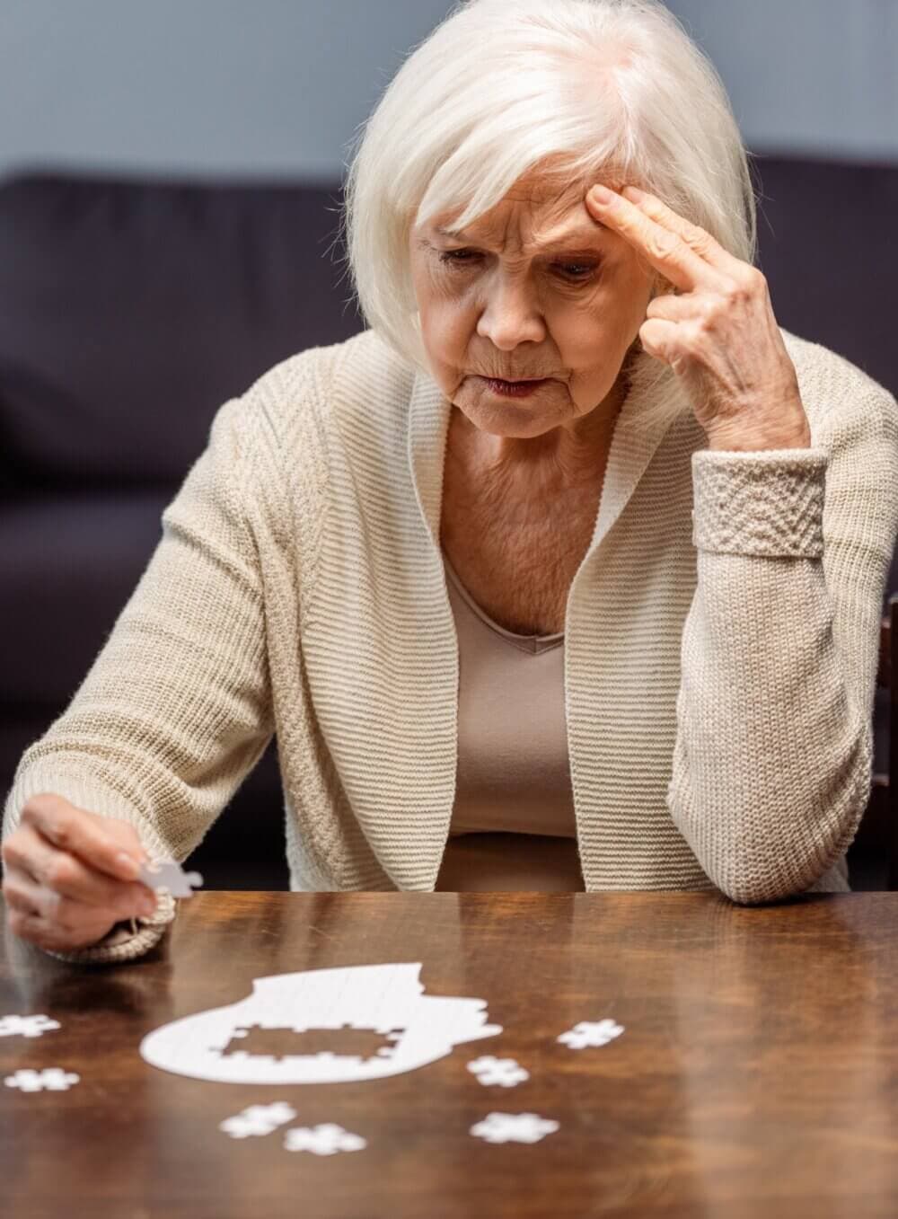 Elderly woman concentrating while solving a jigsaw puzzle at a table. - Home Instead
