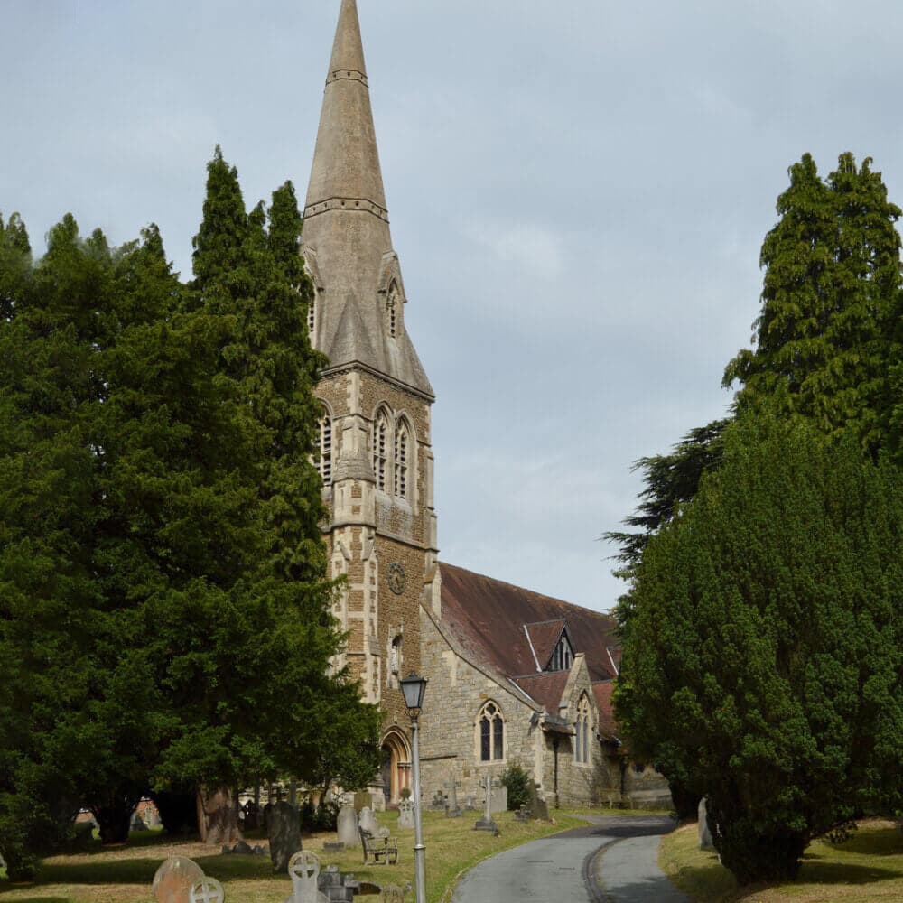 A stone church with a tall steeple, surrounded by trees, and gravestones dotting the foreground. - Home Instead