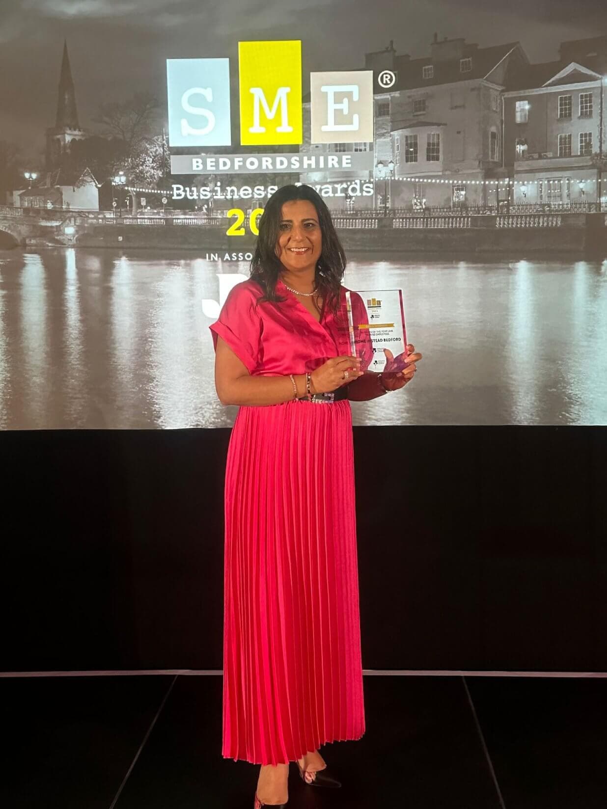 Woman in a pink dress holding an award at the SME Bedfordshire Business Awards event. - Home Instead
