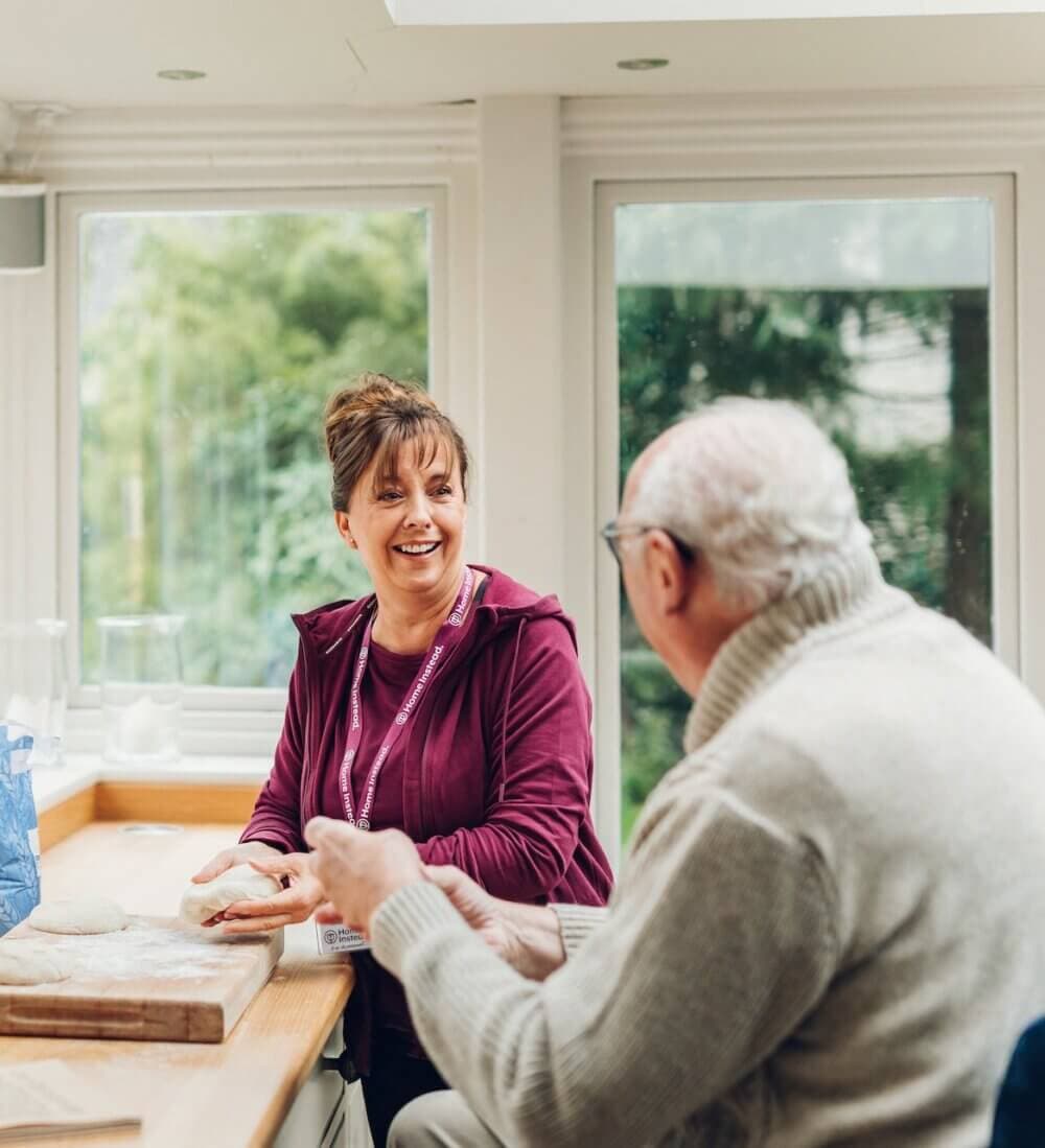 An elderly woman and a younger woman smiling as they look at a tablet together in a cozy living room. - Home Instead