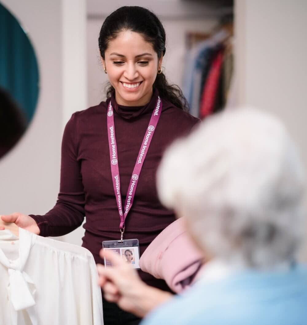 Two men sitting at a table, one showing the other something on a tablet. Coffee and muffins are on the table. - Home Instead