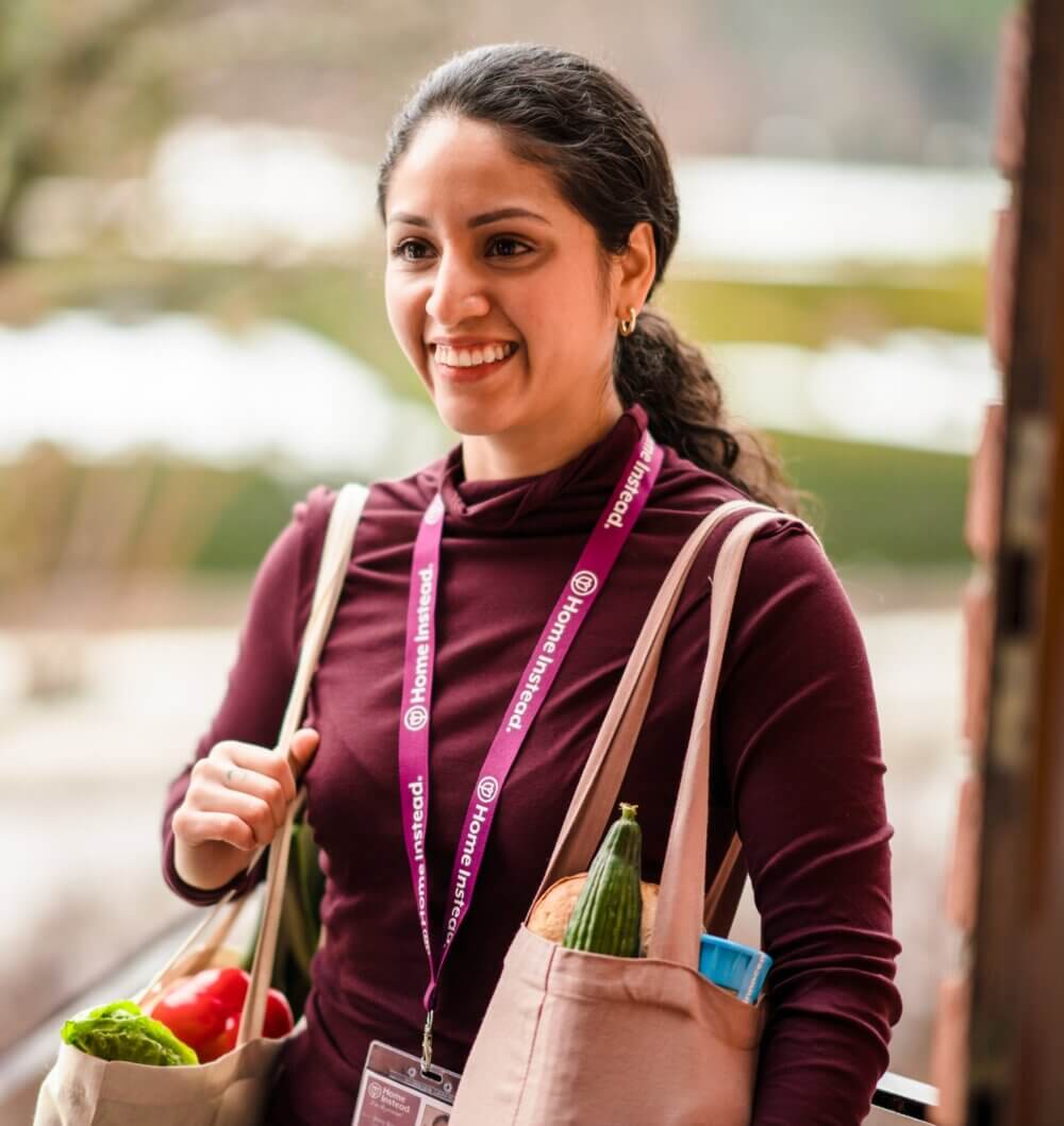 Two women playing chess at a wooden table inside a room with framed artwork on the walls. - Home Instead