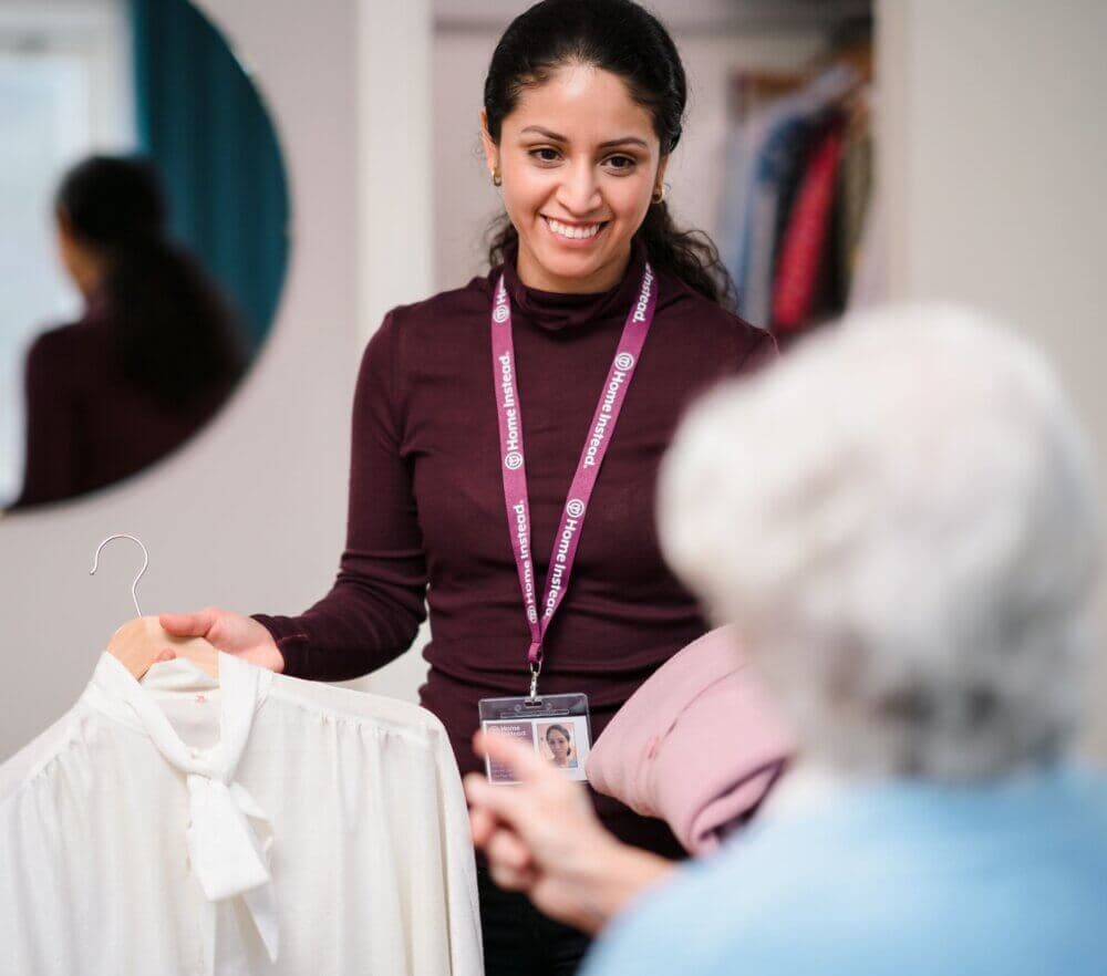A woman and an older man sitting at a table, smiling while looking at a tablet, with coffee and flowers in the foreground. - Home Instead