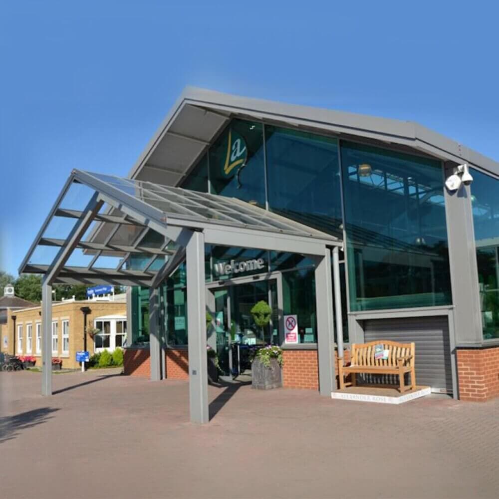 Modern building with glass facade, covered entryway, and a bench outside. Blue sky and additional buildings in view. - Home Instead
