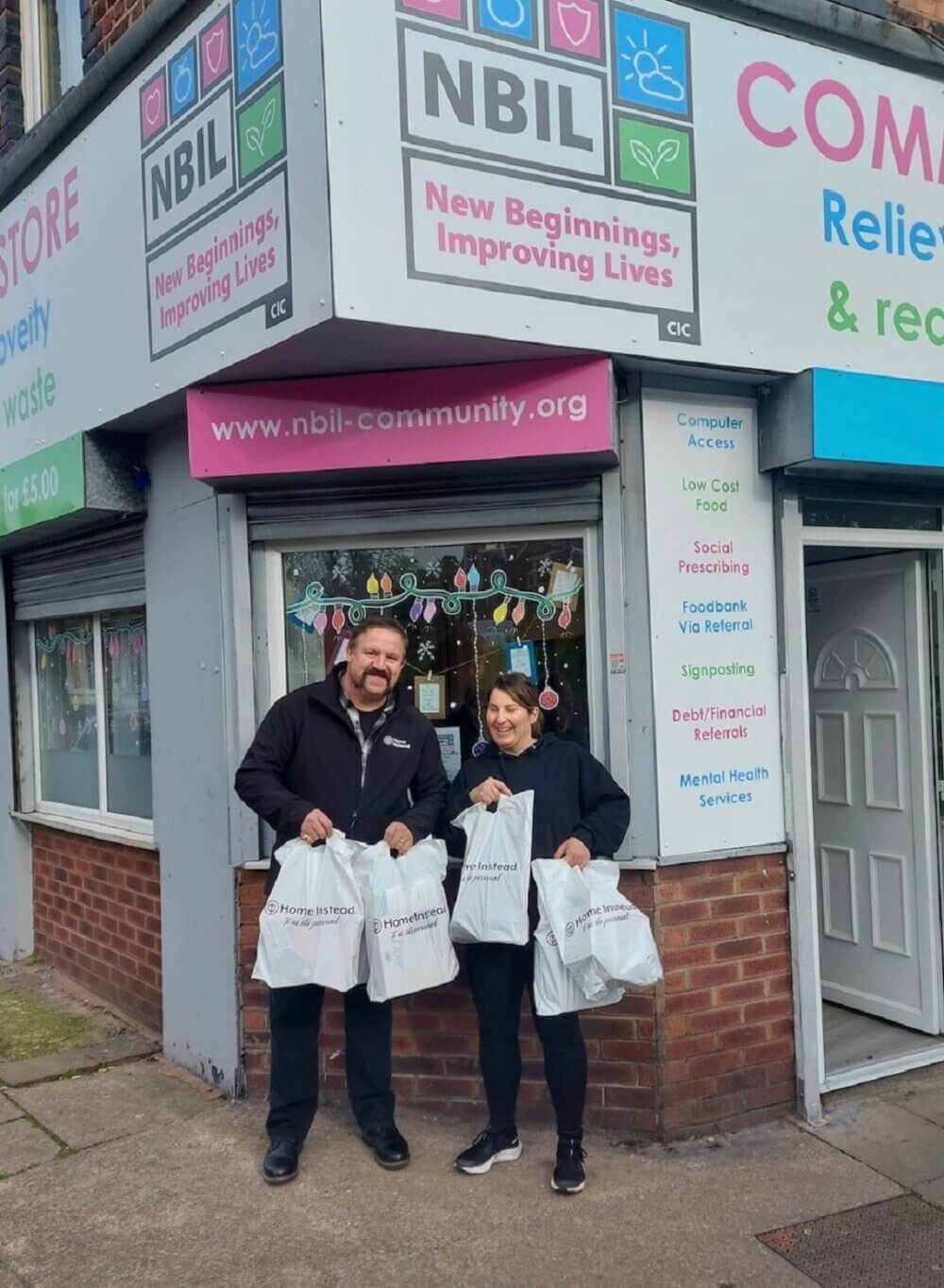 Two people holding shopping bags stand outside NBIL Community Store, which offers various community support services. - Home Instead