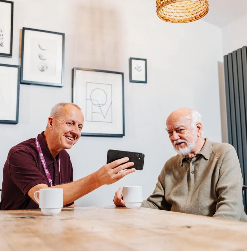 A caregiver in a purple top brushes the hair of an elderly person sitting in a well-lit room with large windows. - Home Instead