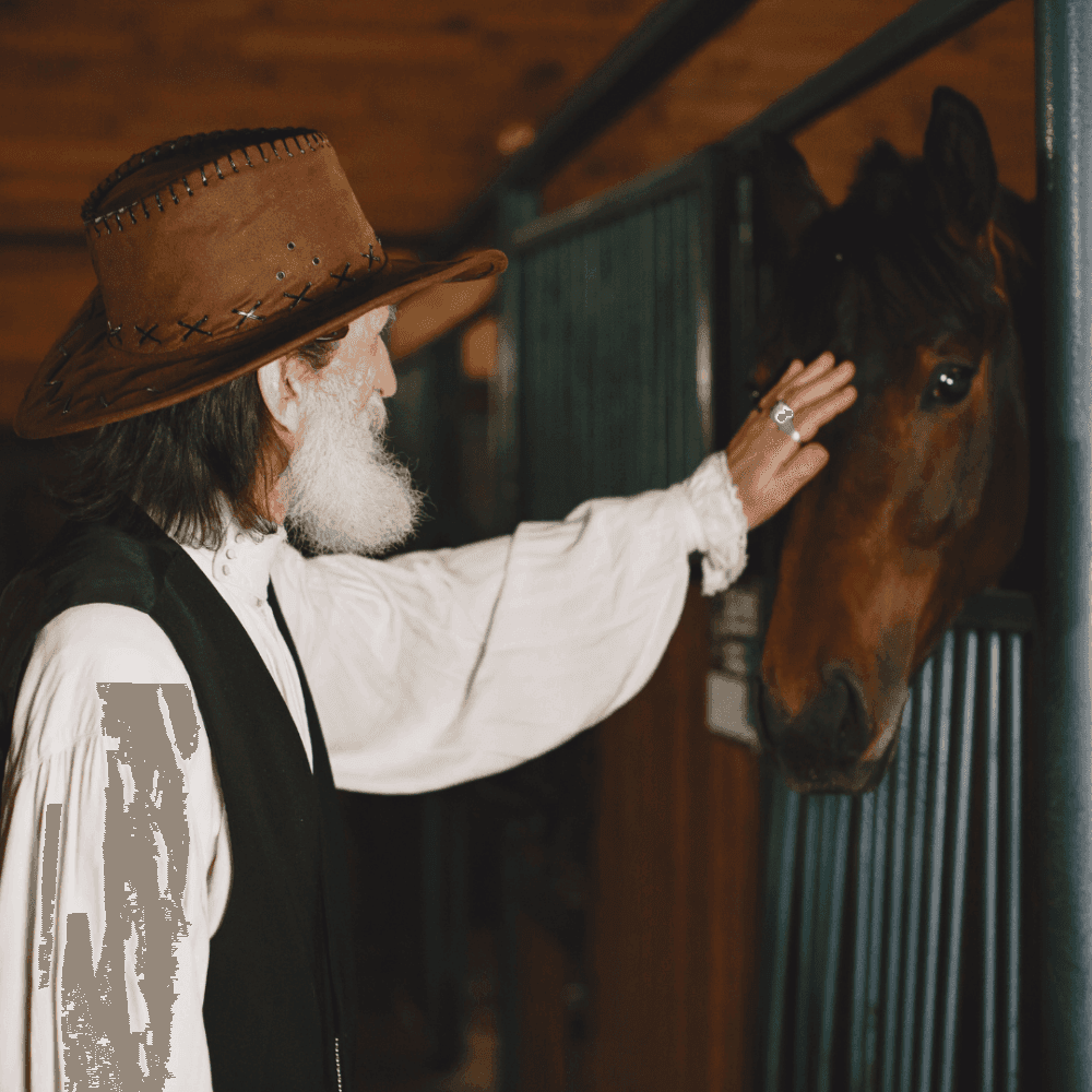 An older man wearing a wide-brimmed hat gently pats a horse in a stable. - Home Instead