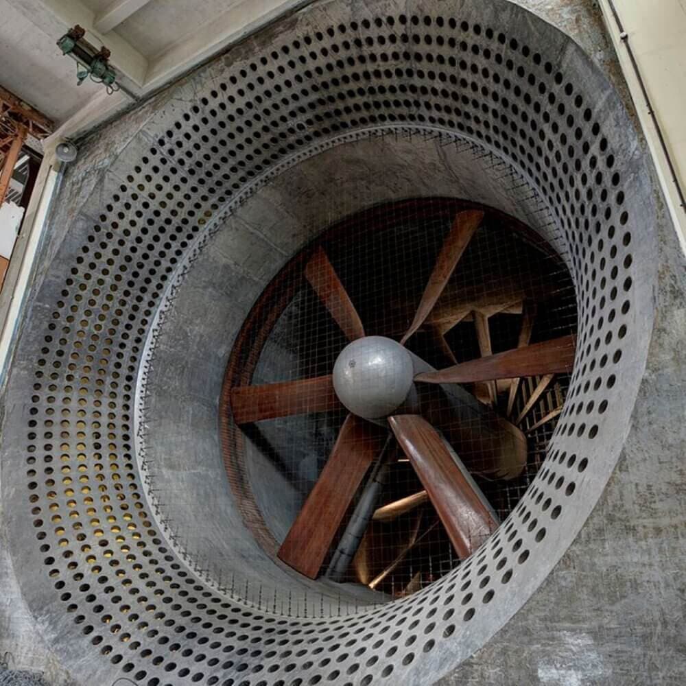 Large industrial fan with wooden blades inside a perforated metal casing, visible from a front-facing angle. - Home Instead