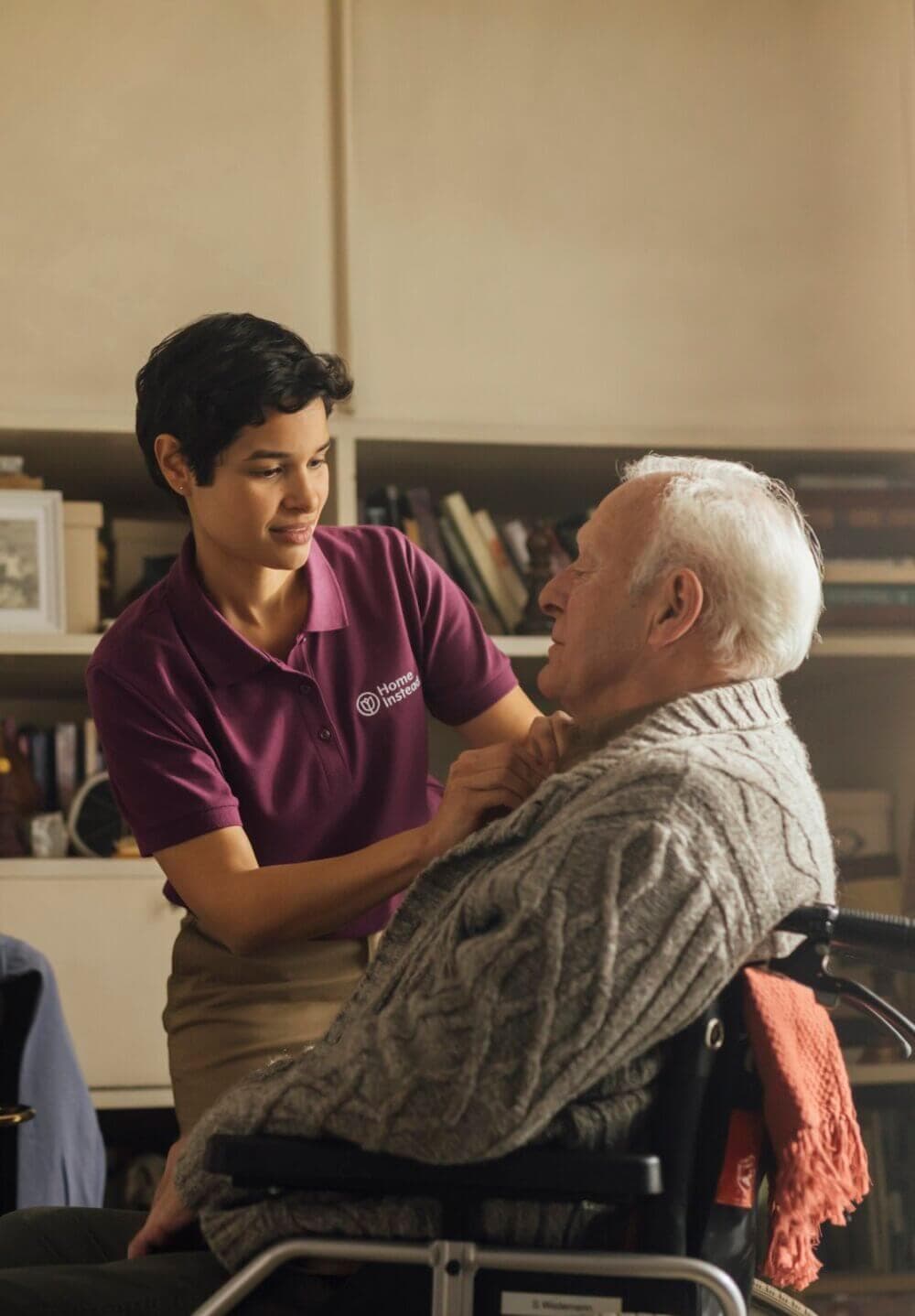 A smiling young woman helps an older woman with laundry on a drying rack, both wearing light pink tops. - Home Instead