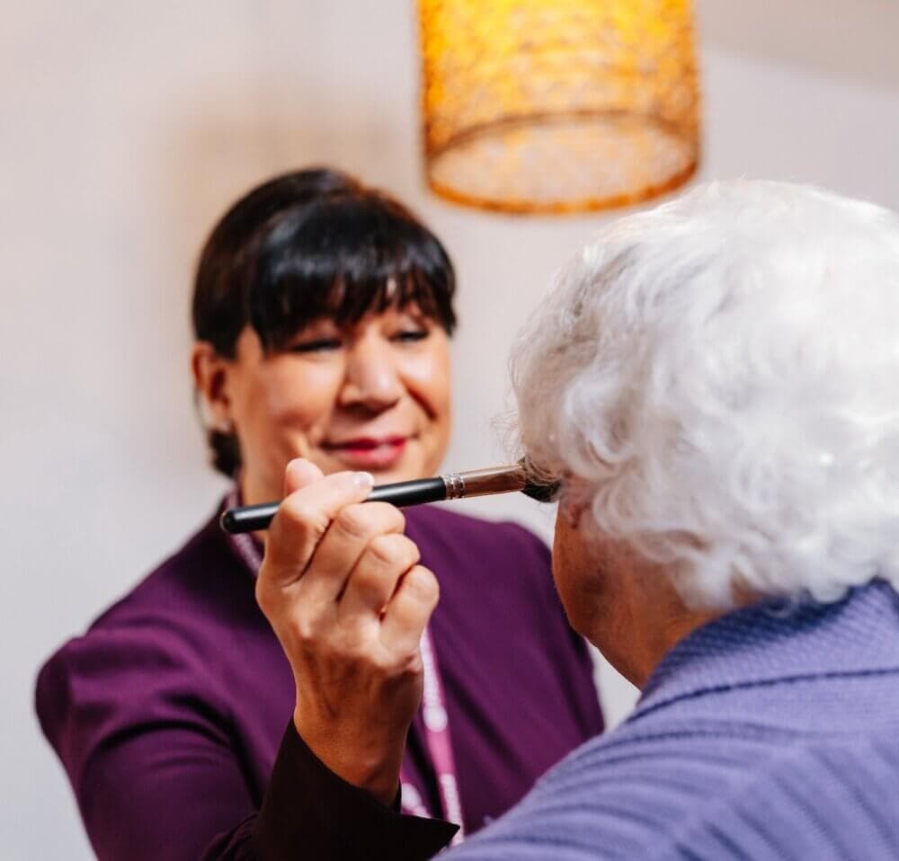 Two women smiling and playing a keyboard together against a wooden wall background. - Home Instead