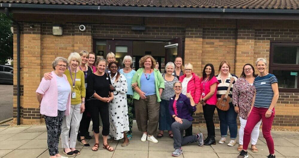 Group of smiling adults in casual clothing posing in front of a brick building. - Home Instead