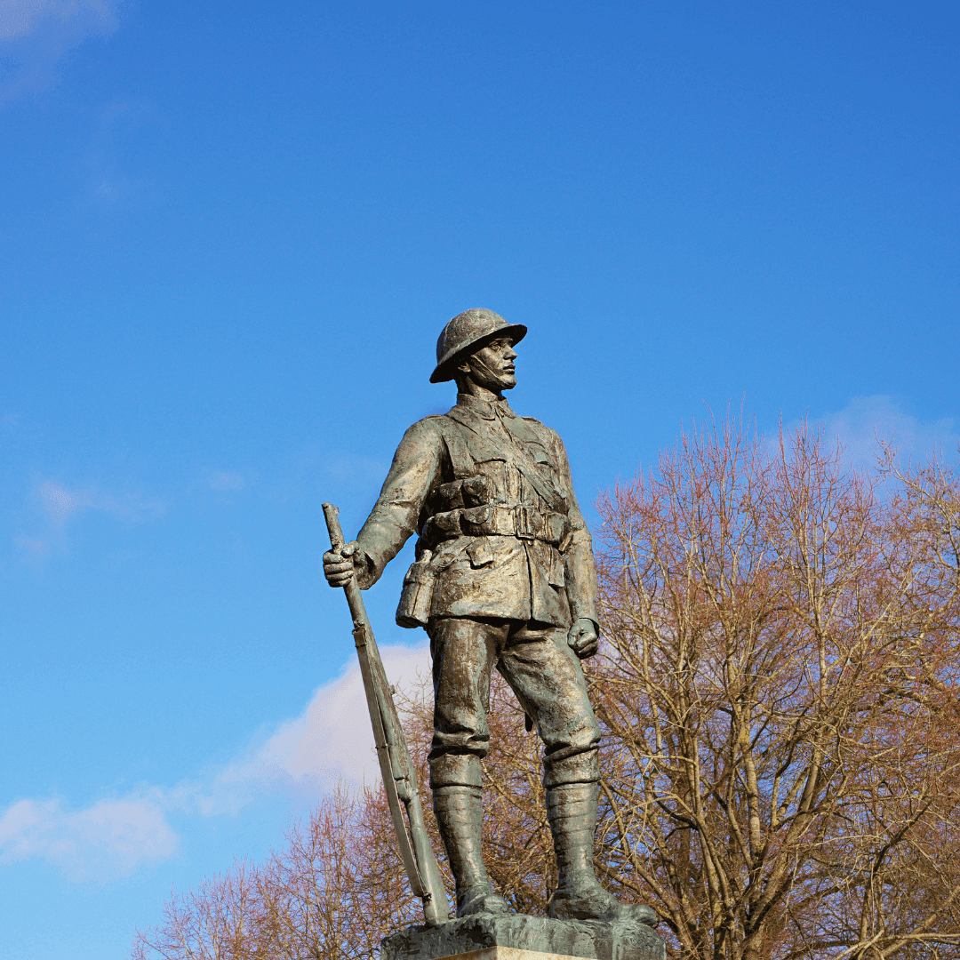 A bronze statue of a soldier in uniform holding a rifle, against a backdrop of clear blue sky and bare trees. - Home Instead