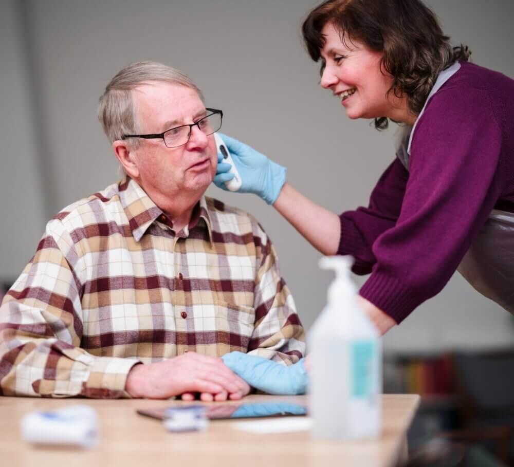 A caregiver wearing a name tag brushes the hair of an elderly person with long white hair in a bright room. - Home Instead