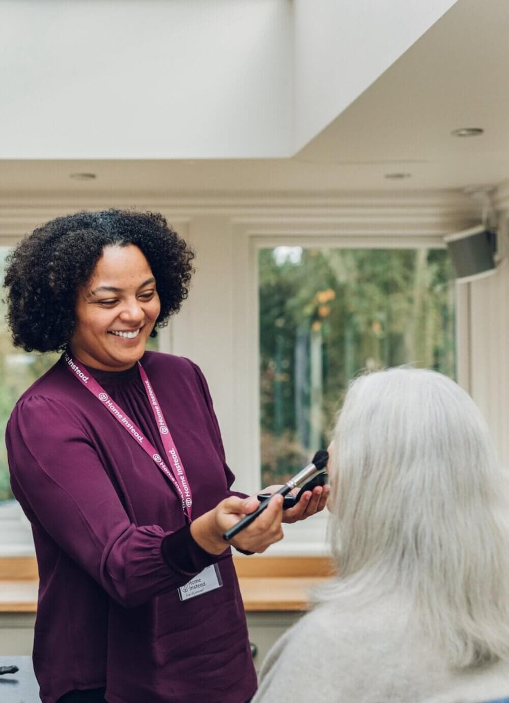 Home Instead Poole Care Professional applying makeup to a seated person with white hair.
