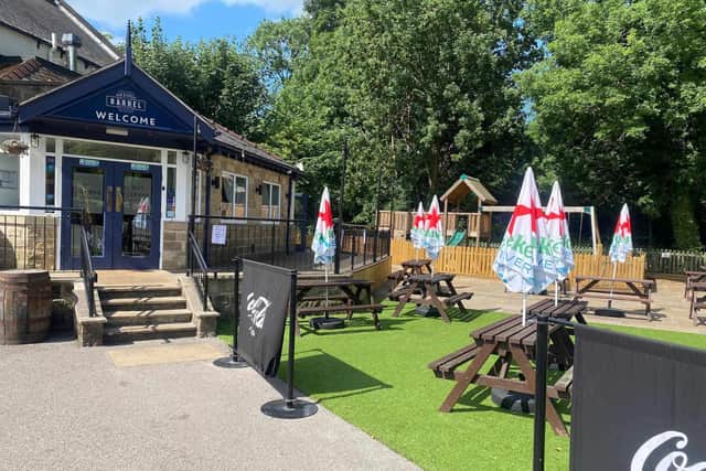Outdoor seating area of a pub with picnic tables, parasols, and a children's play area, surrounded by greenery. - Home Instead