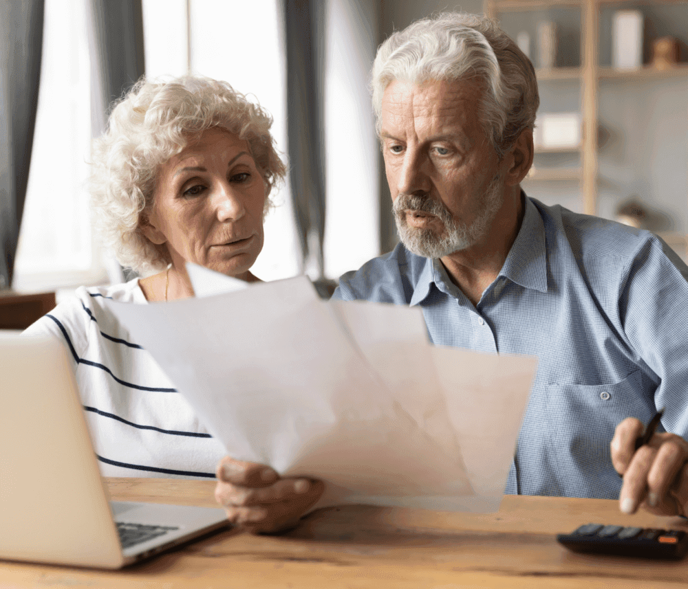 Elderly couple reviewing documents at a table with a laptop and calculator. - Home Instead