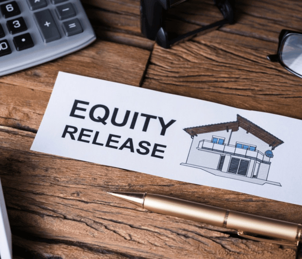 Paper with "Equity Release" text and house illustration on a wooden desk, surrounded by a pen, calculator, and glasses. - Home Instead