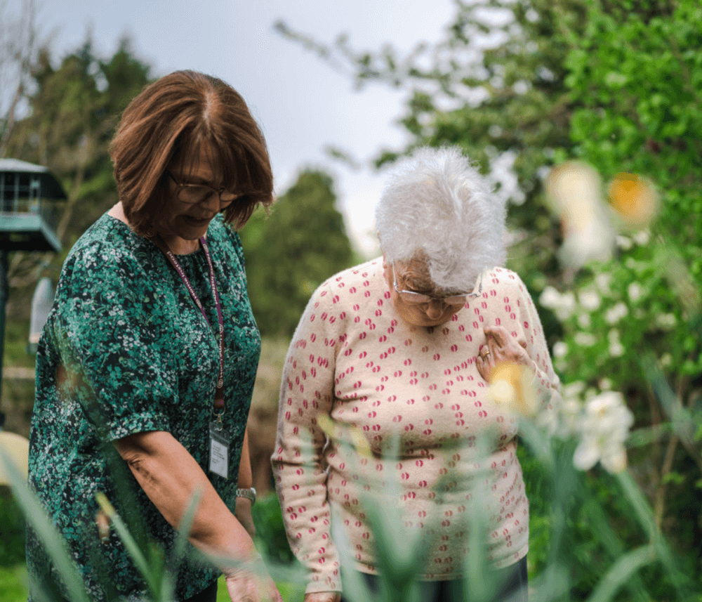 Two women, one elderly and one younger, tending to a garden together on a bright day. - Home Instead