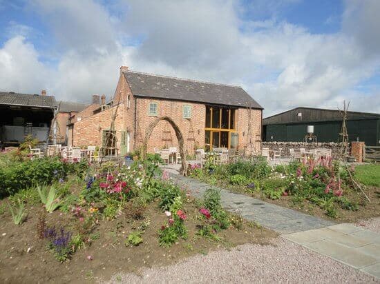 Brick building with large windows, surrounded by a garden with flowers and a stone pathway, set against a cloudy sky. - Home Instead
