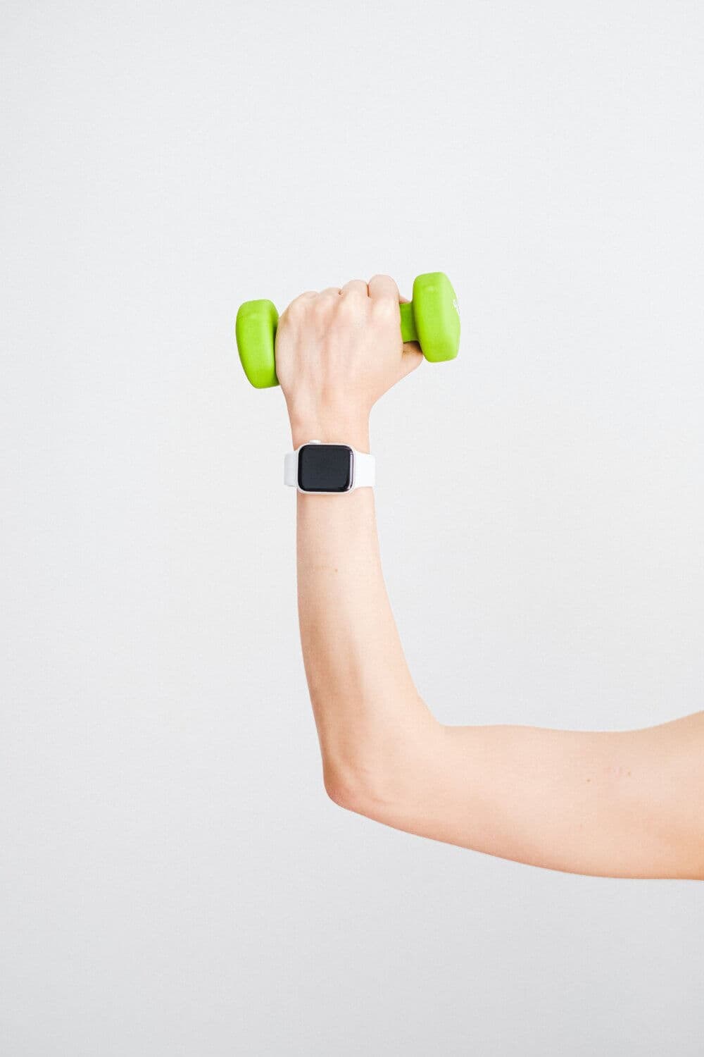 A hand lifting a green dumbbell in the air, wearing a smartwatch on the wrist. - Home Instead