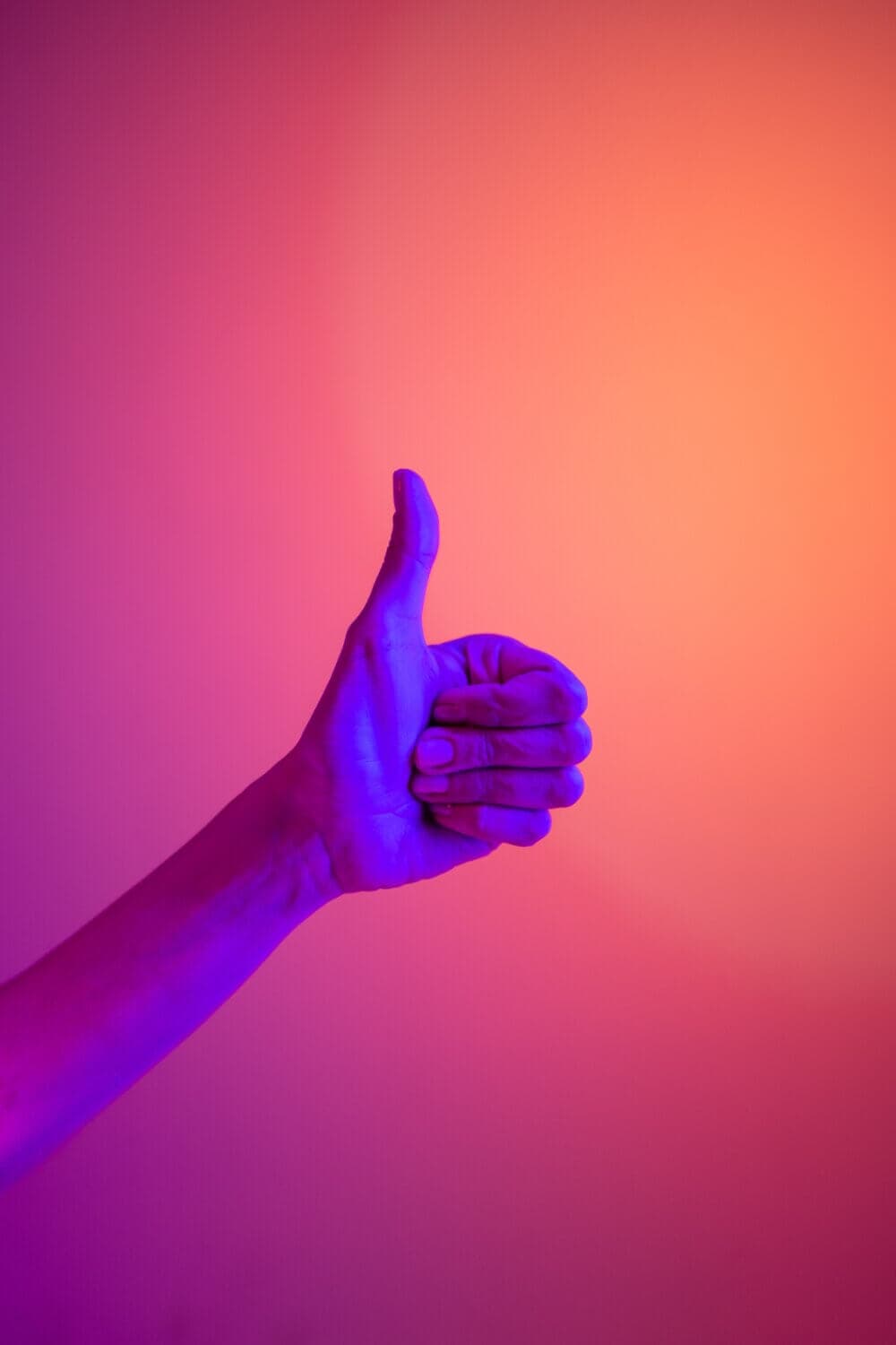 A hand giving a thumbs-up gesture is illuminated with purple and pink lighting against a gradient background. - Home Instead