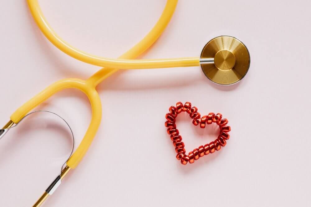 Yellow stethoscope with a red beaded heart on a light pink background. - Home Instead
