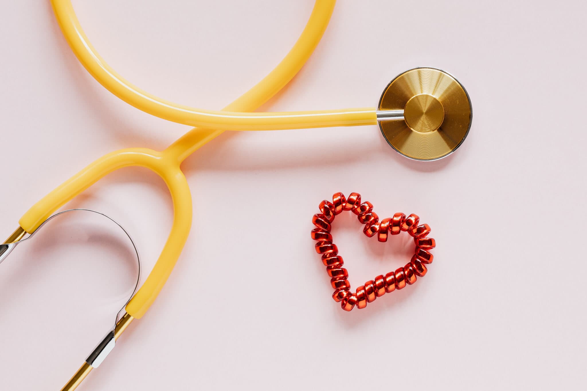 Yellow stethoscope with a red beaded heart on a light pink background. - Home Instead