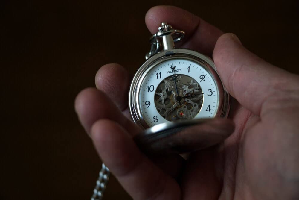 Close-up of a hand holding an open pocket watch, showing its intricate inner gears and classic numbered dial. - Home Instead