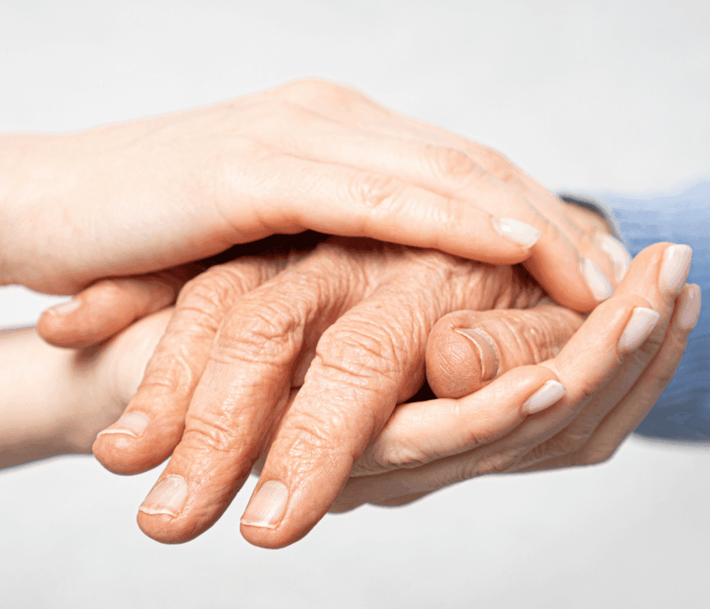 An elderly hand held gently by two young hands against a neutral background, symbolizing care and support. - Home Instead