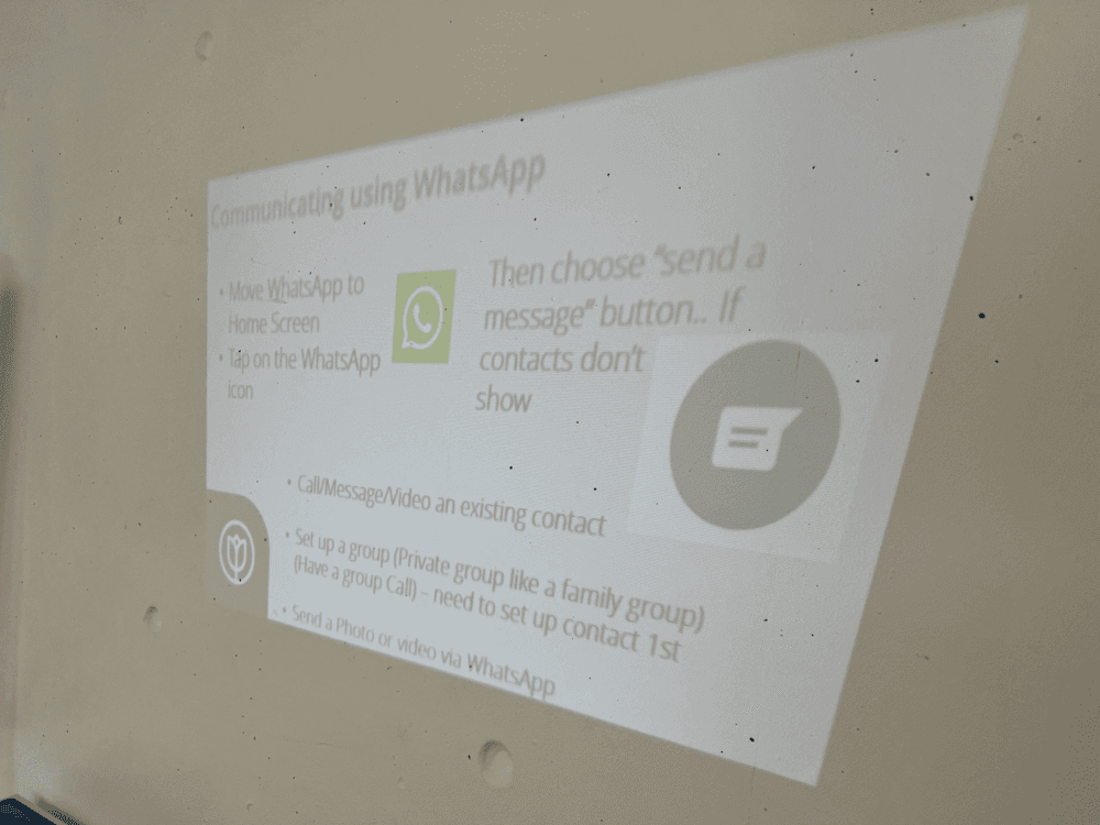 A projector screen displaying instructions for using WhatsApp, including setting up a group and sending messages. - Home Instead