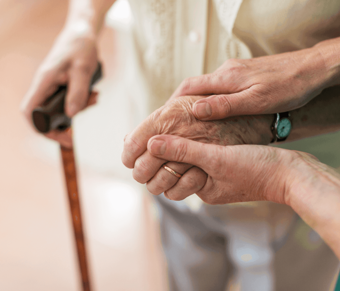 Close-up of a caregiver holding an elderly person's hand, with the elderly person holding a wooden cane in the other hand. - Home Instead