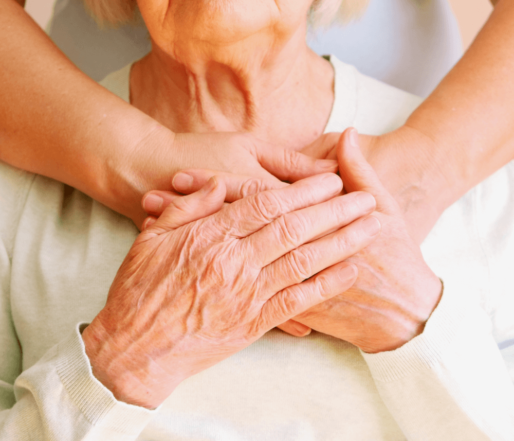 An elderly person being comforted by a younger person's hands, with both pairs of hands resting together. - Home Instead