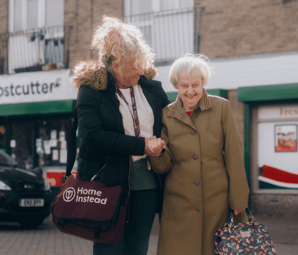 Two women holding hands and walking on a sidewalk. - Home Instead