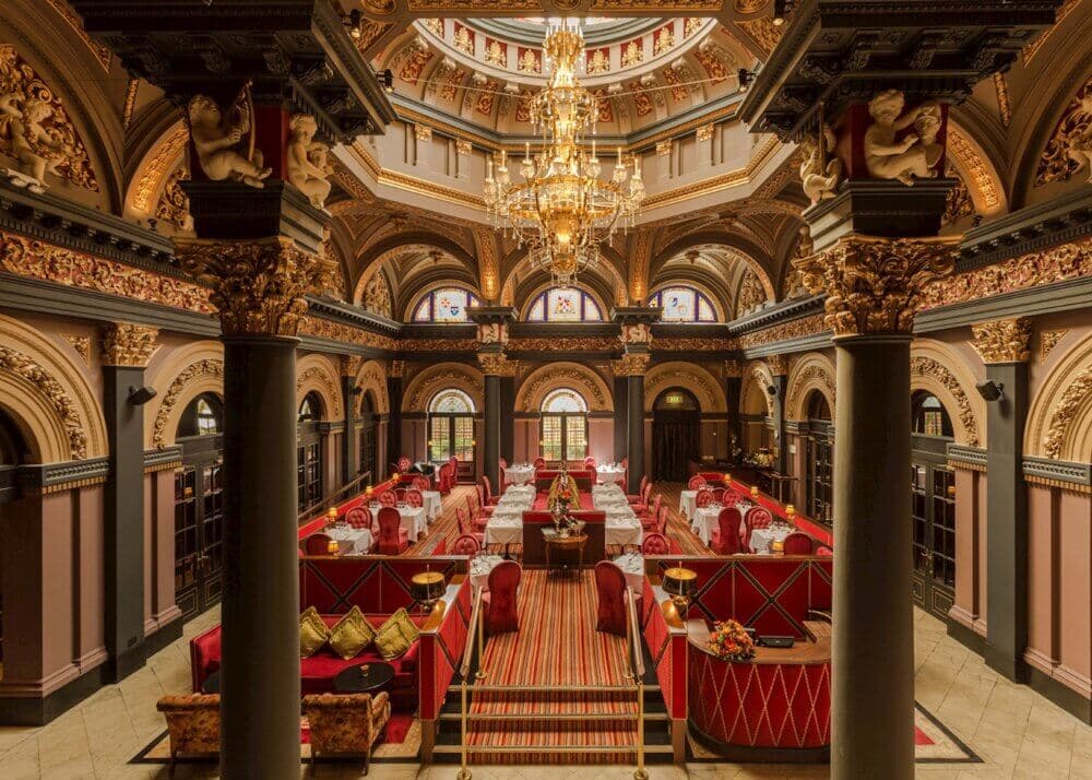 Luxurious, ornate dining hall with tall columns, intricate carvings, red seating, and an elegant chandelier. - Home Instead