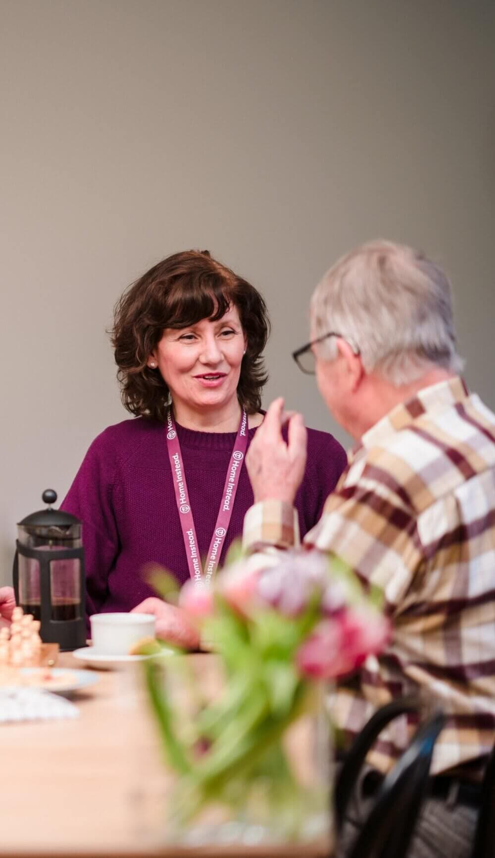 Two men sitting at a table with coffee, smiling at a smartphone one of them is holding up. Art frames on the wall. - Home Instead