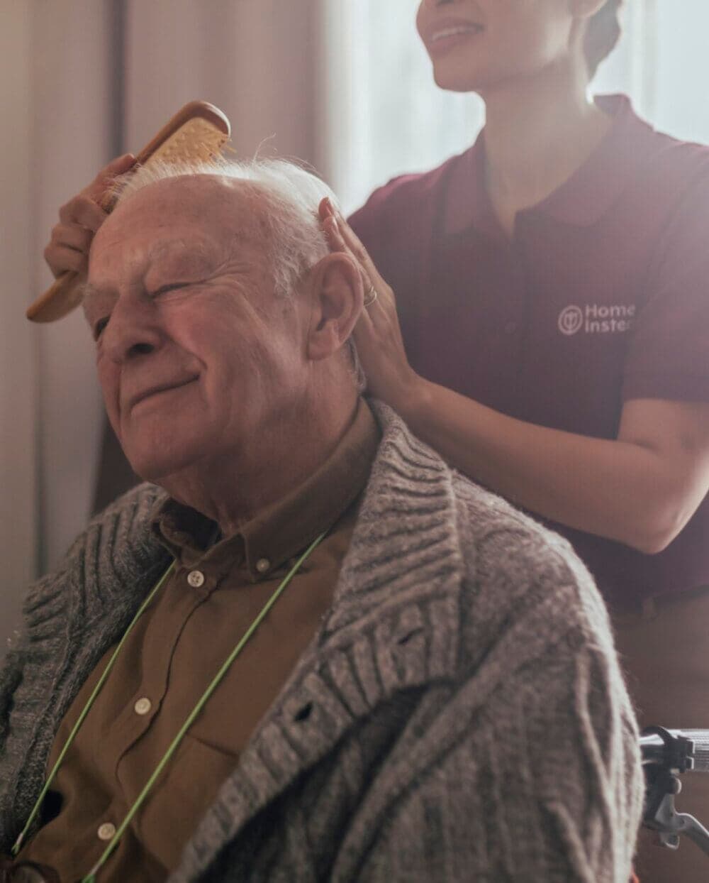 A Care Professional gently brushes the hair of an elderly man who is sitting and smiling, creating a warm and comforting scene. - Home Instead Southampton