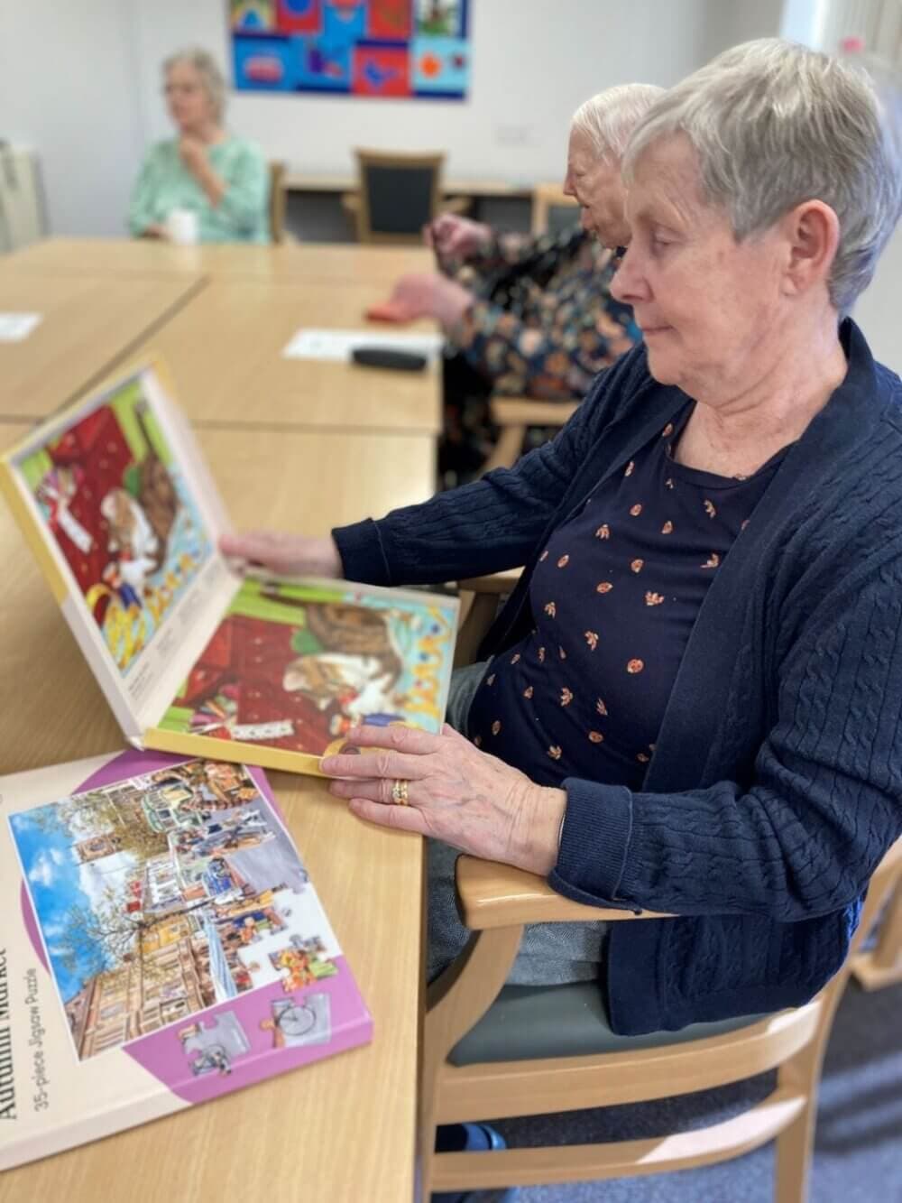 Elderly women reading books at a table, with colorful books spread out on the table in a communal setting. - Home Instead