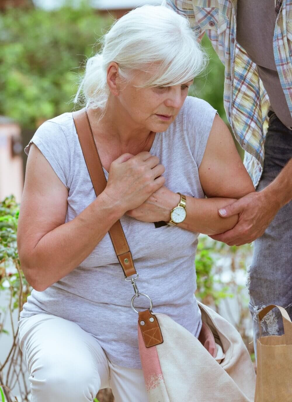 Elderly woman clutching her chest while a person assists her, appearing concerned outdoors. - Home Instead Bournemouth & Christchurch