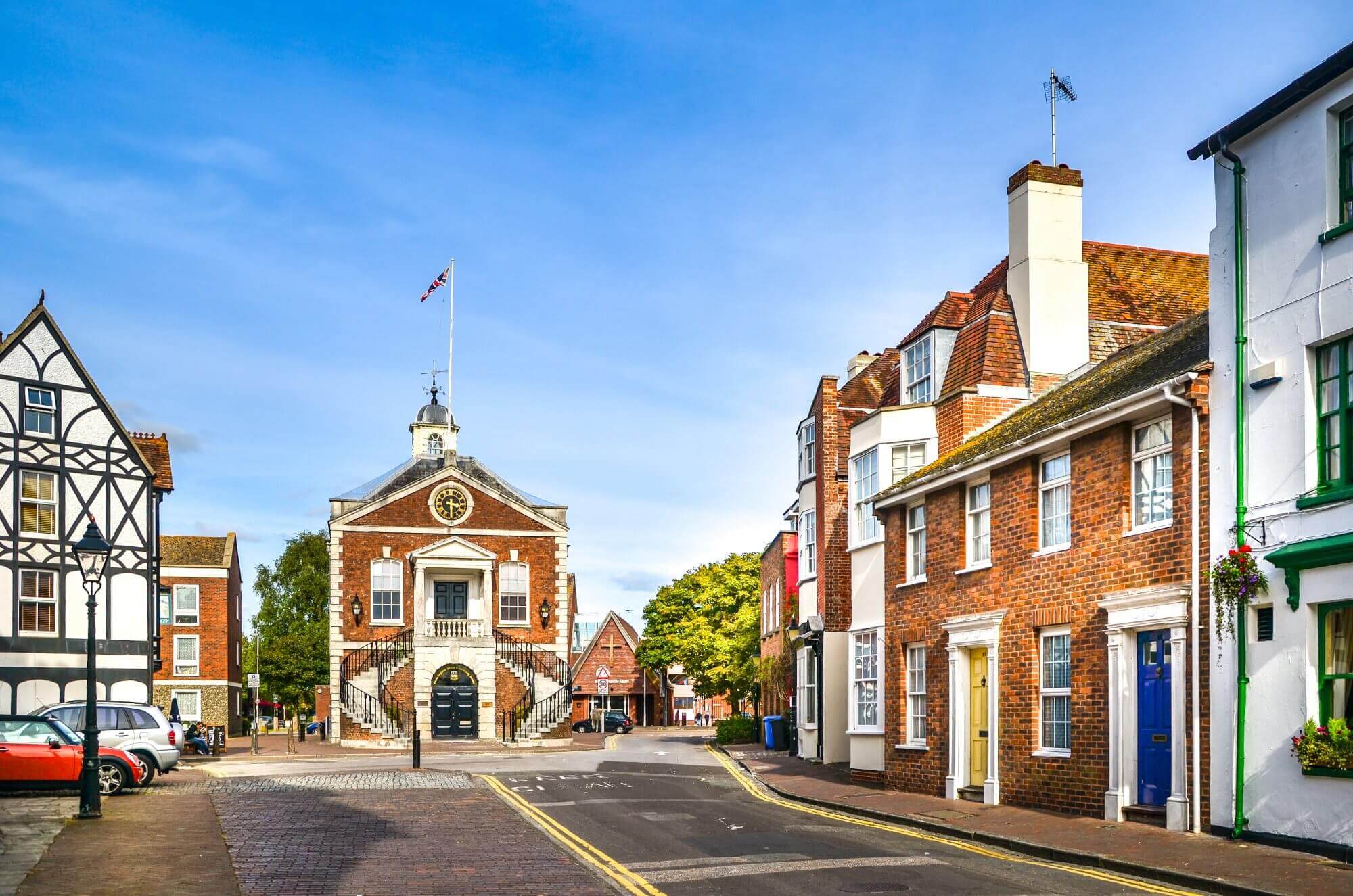 Quaint village street with colorful houses and a historic building with a clock tower under a clear blue sky. - Home Instead Poole